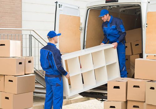 Young male movers unloading furniture and cardboard boxes from truck on street